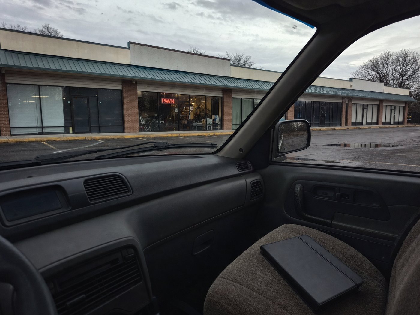 Inside a parked car, looking out at a strip of shops.